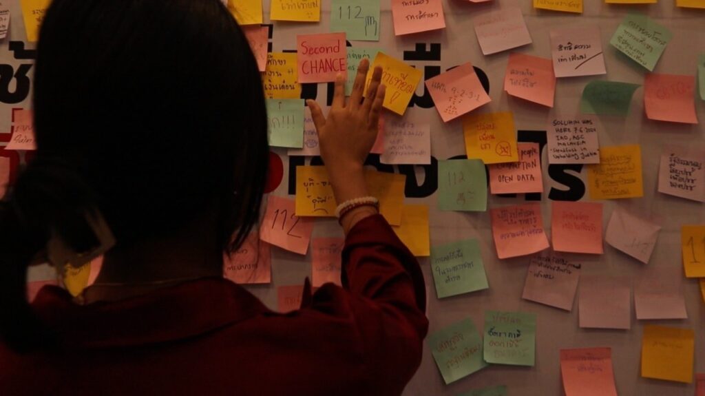 A student reaches out to place a sticky note reading "Second Chance" on a colorful wall filled with handwritten messages and ideas, symbolizing hope, reintegration, and the collaborative effort behind the award-winning BAScii film "Second Chance."